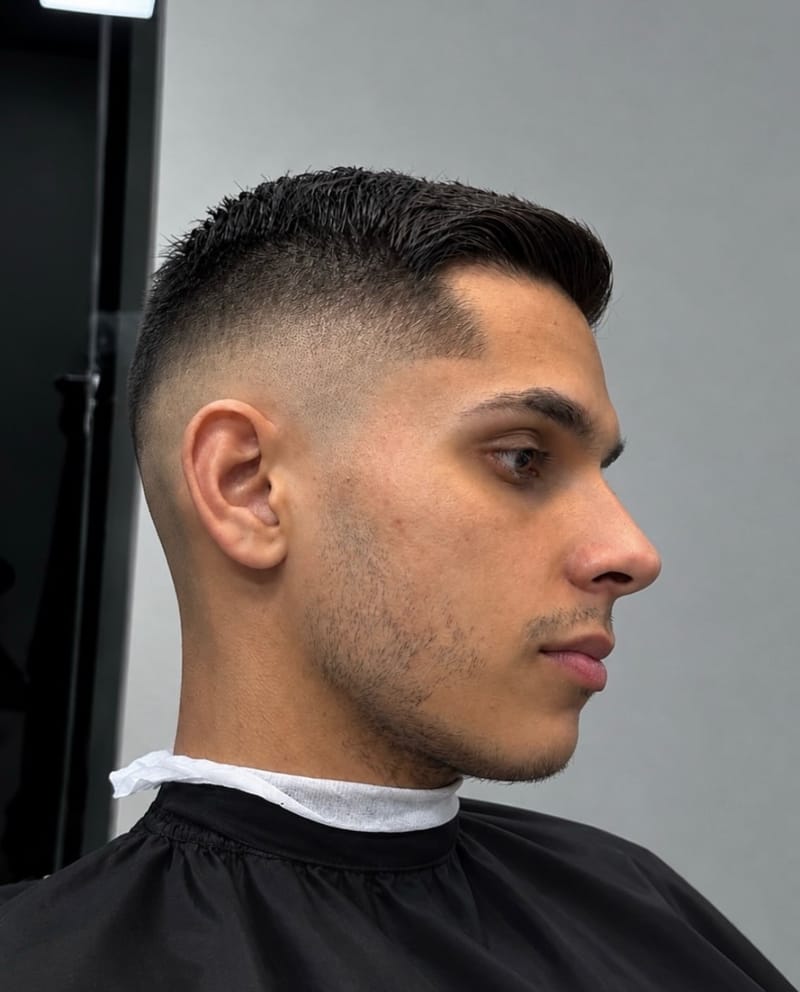 Cliente de perfil com o topo curto penteado para cima e as laterais bem rentes, clareando até a pele perto da orelha.