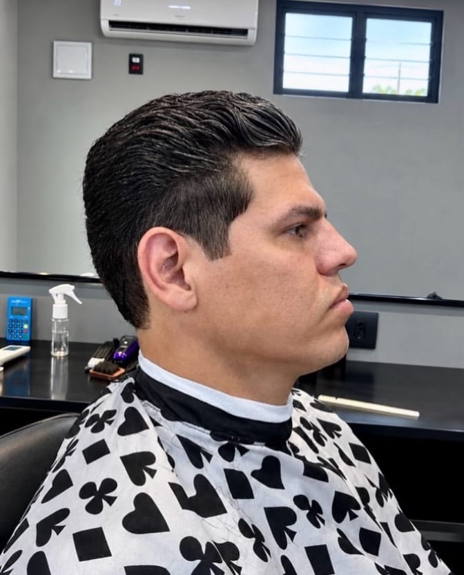 Cliente de perfil com cabelo volumoso penteado para trás e laterais curtas, usando capa estampada com naipes de baralho.